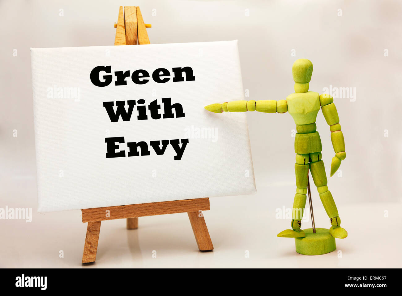 Wooden man with white board pointing at words "Green with envy" jealous jealousy envious wanting wants Stock Photo