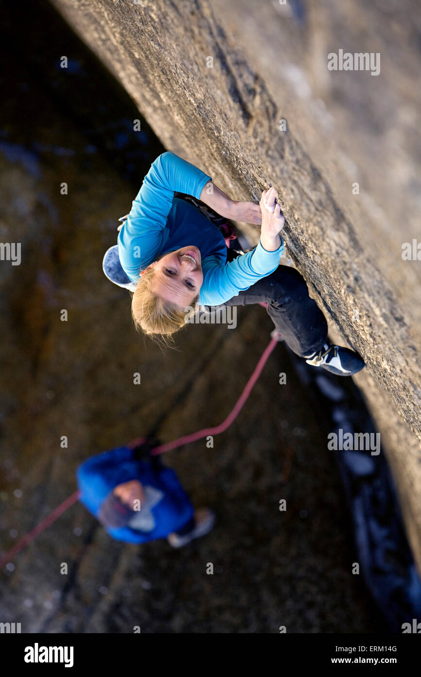 Woman climbing a small crack above her belay partner and a river in Yosemite National Park, California. Stock Photo