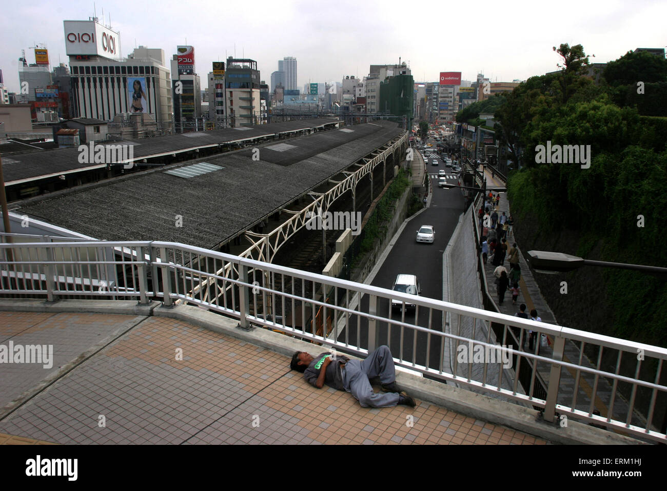 A homeless man sleeps on a sidewalk with the back drop of Tokyo buildings, Japan. Stock Photo