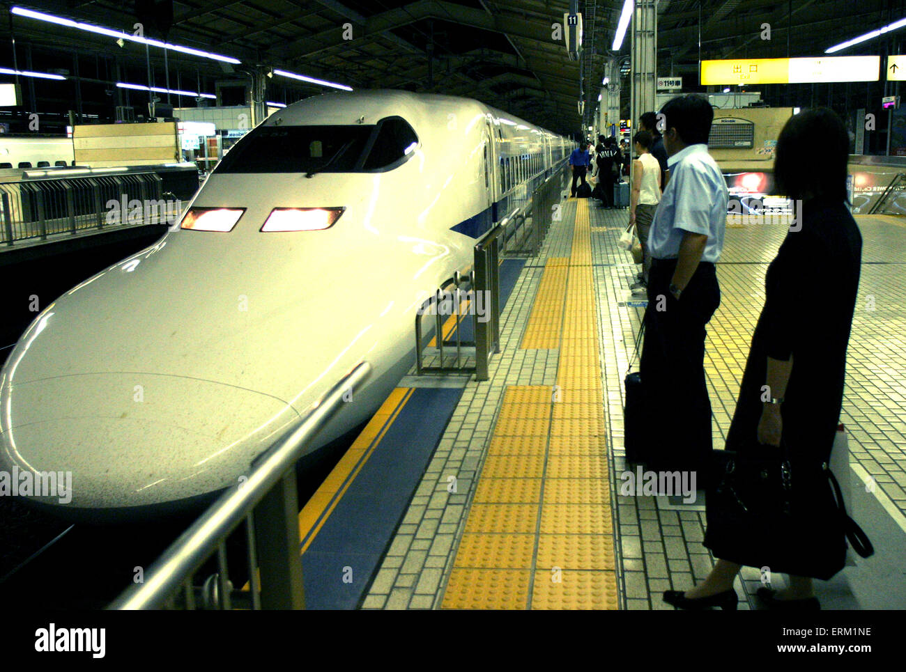 Several people wait to board the 200 mph Shinkansen or 'Bullet Train' in a Tokyo train station, Japan. Stock Photo