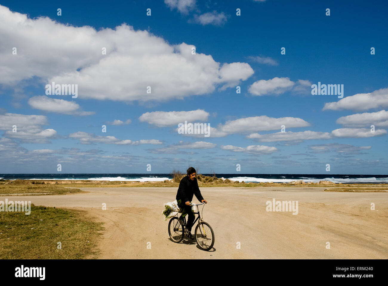 A Cuban man rides a bicycle on the dusty road along the sea in Alamar, Havana, Cuba. Stock Photo
