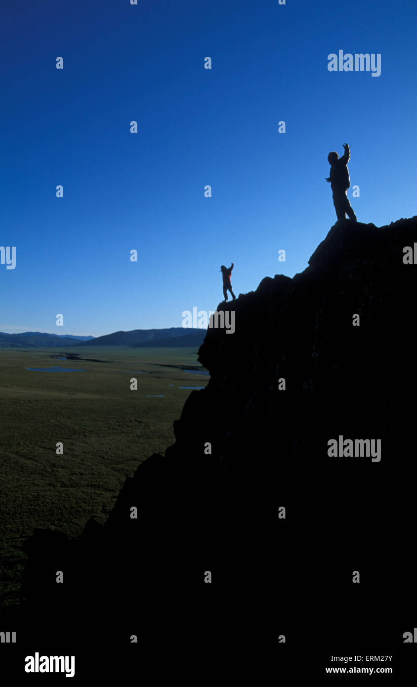 Two people stand on the edge of a cliff with their arms raised near Firth River in Yukon Territories, Canada. Stock Photo