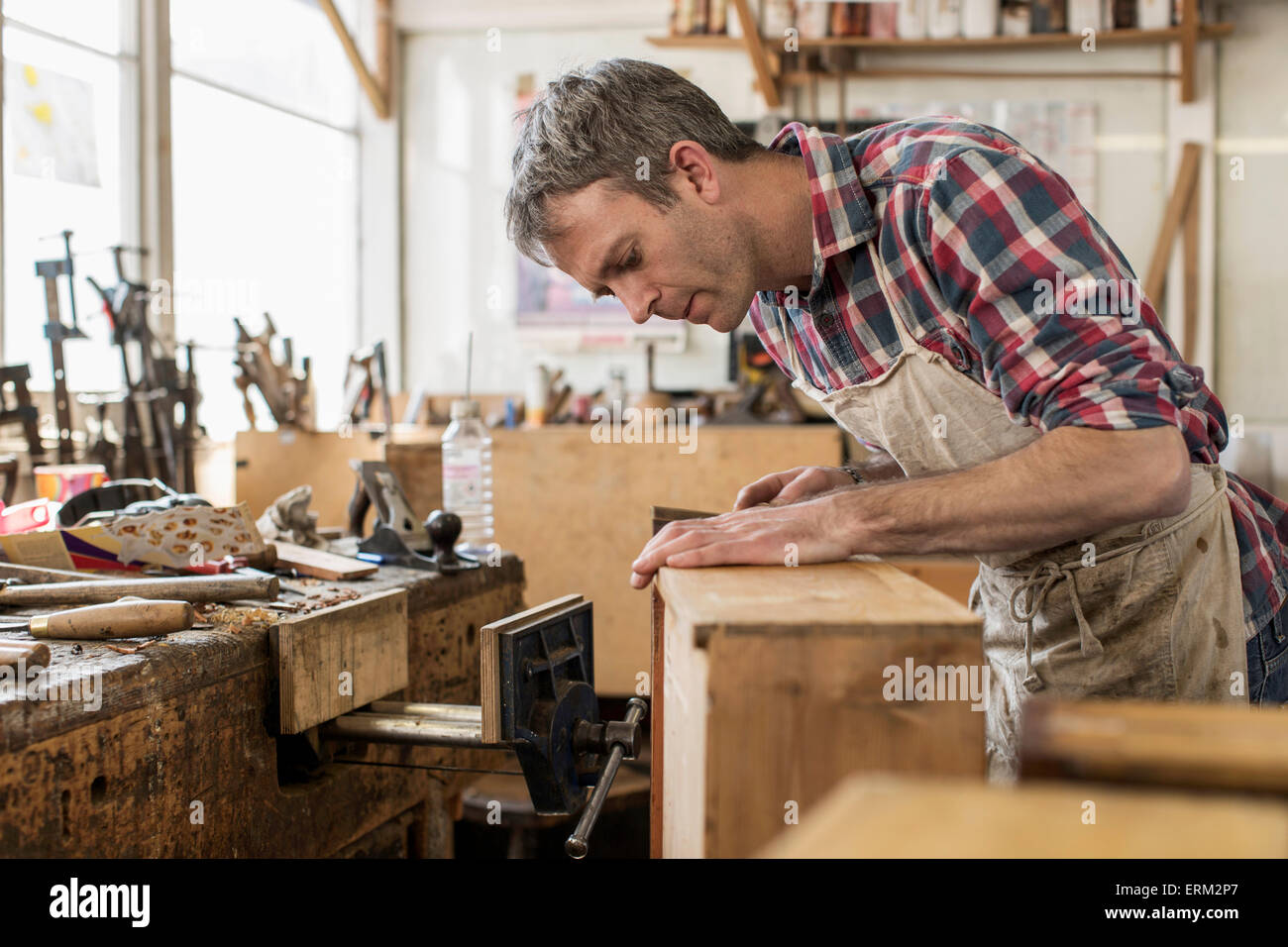 An antique furniture restorer in his workshop using a hand tool to smooth a wooden object. Stock Photo