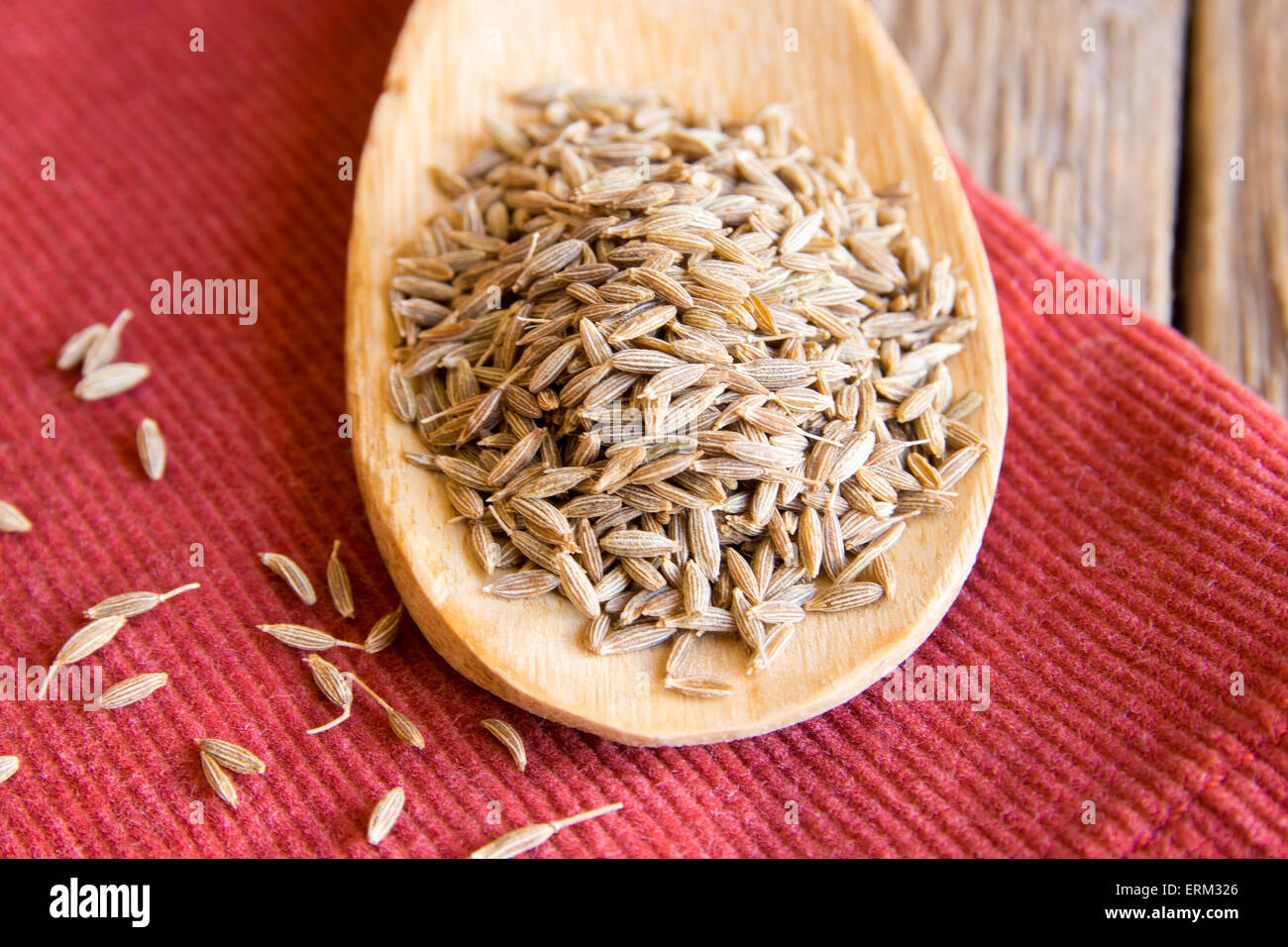 cumin seeds on wooden spoon over red napkin, close up Stock Photo