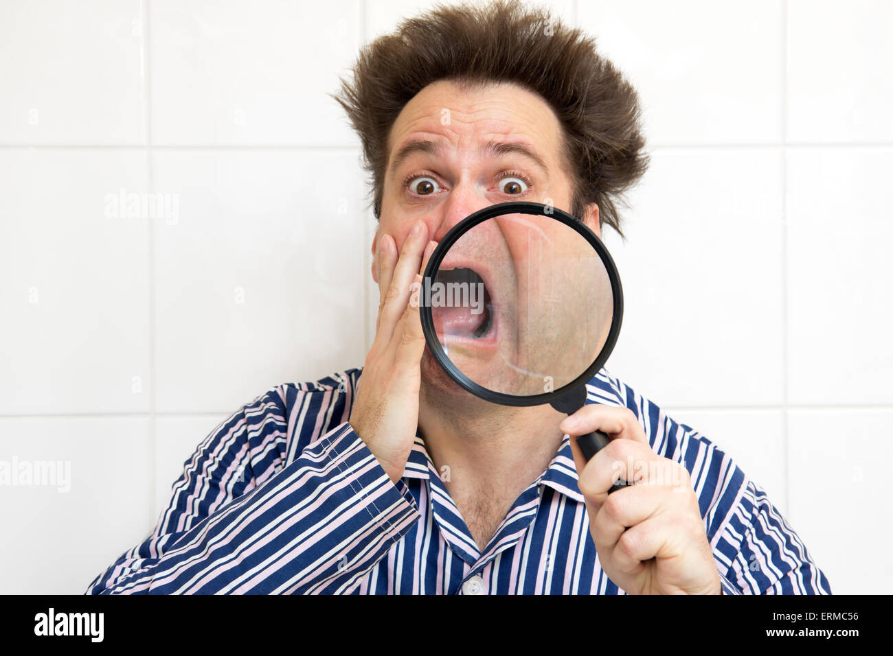 frightened man in pajamas watching his face magnifying glass Stock Photo