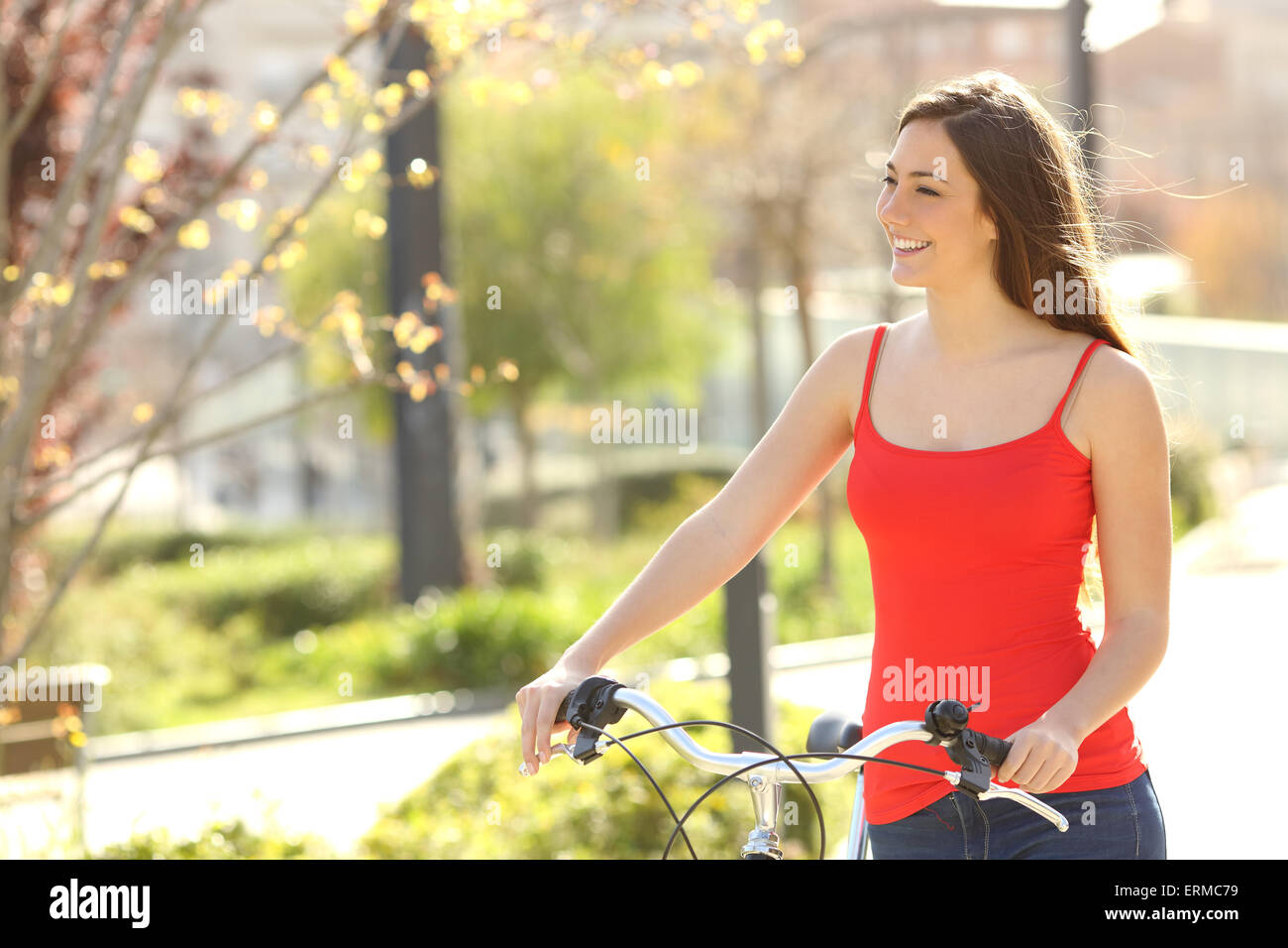 Candid woman walking in an urban park in summer or spring carrying a bicycle Stock Photo