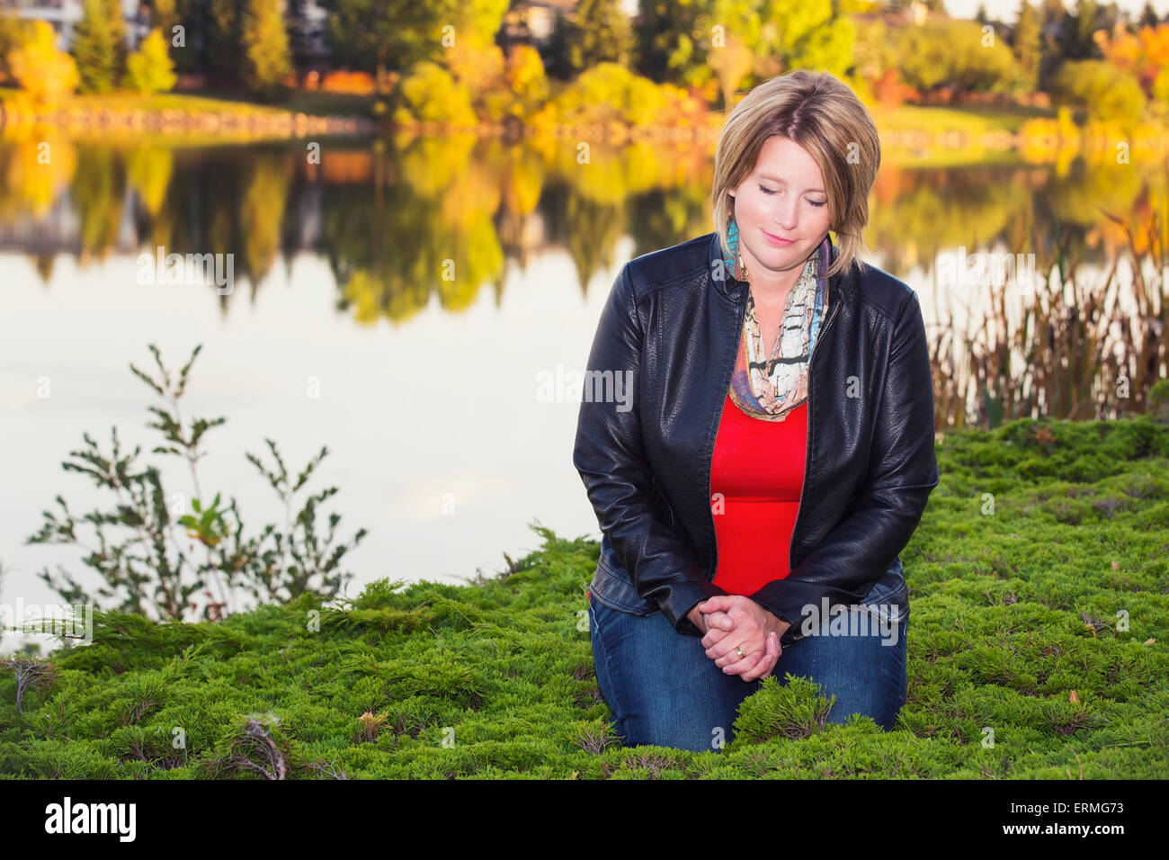 Mature Christian Woman Kneeling And Praying Beside A Lake In Autumn Edmonton Alberta Canada