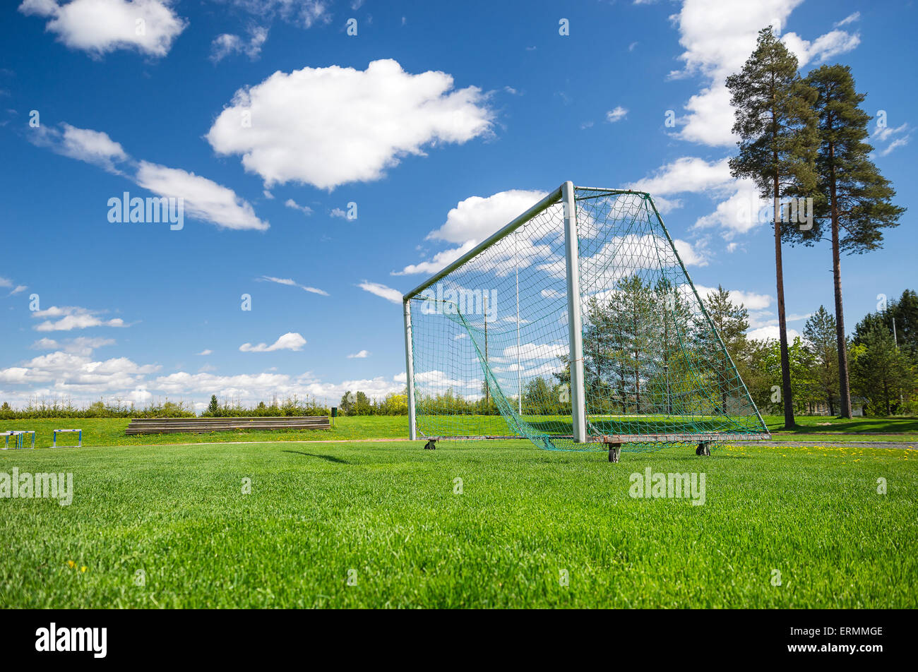 Soccer field and empty net against blue sky and white clouds Stock