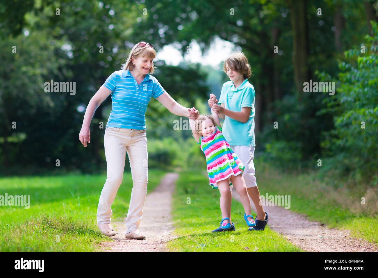 Happy active woman enjoying hiking with two children, school age boy and cute curly toddler girl walking in pine wood forest Stock Photo