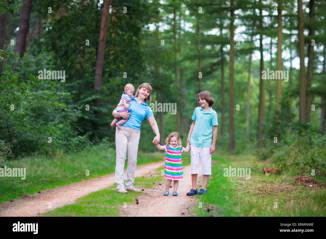 Happy active woman enjoying hiking with three children, school age boy, toddler girl and little baby, walking pine wood forest Stock Photo