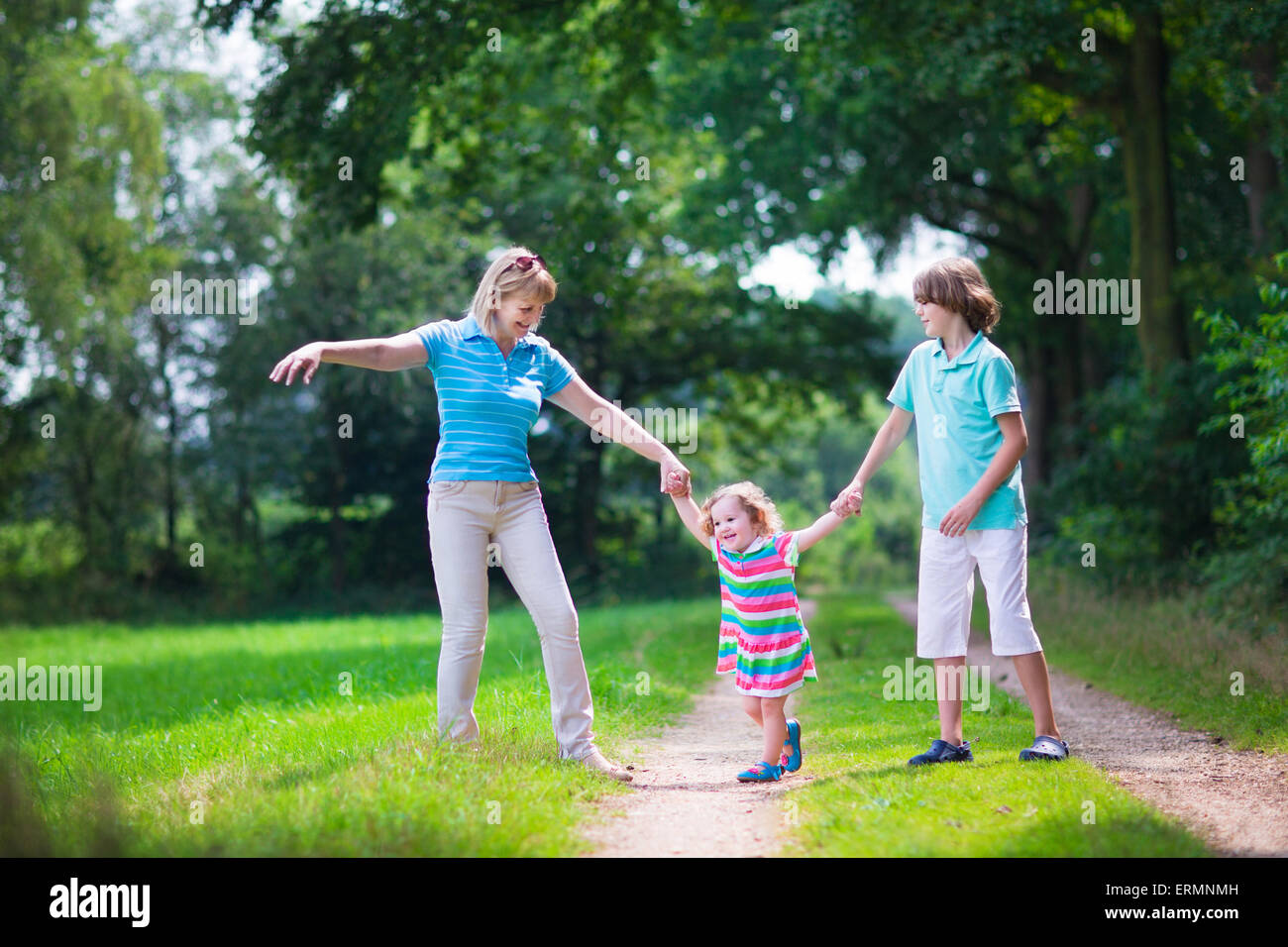 Happy active woman enjoying hiking with two children, school age boy and cute curly toddler girl walking in pine wood forest Stock Photo