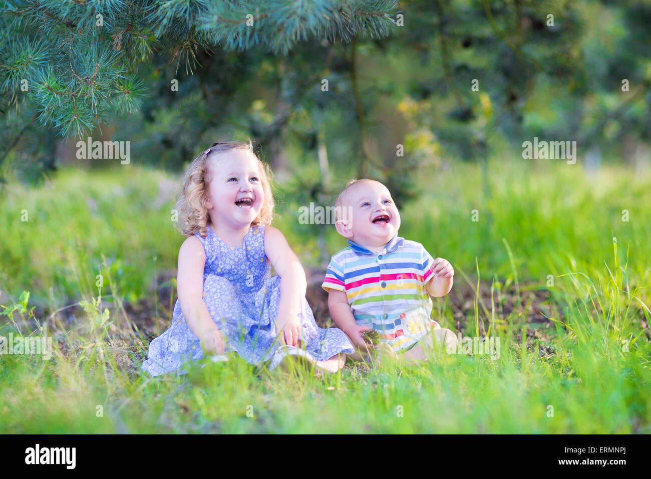 Happy little children, adorable toddler girl in a blue dress and a cute baby boy, brother and sister, playing with pine cones Stock Photo