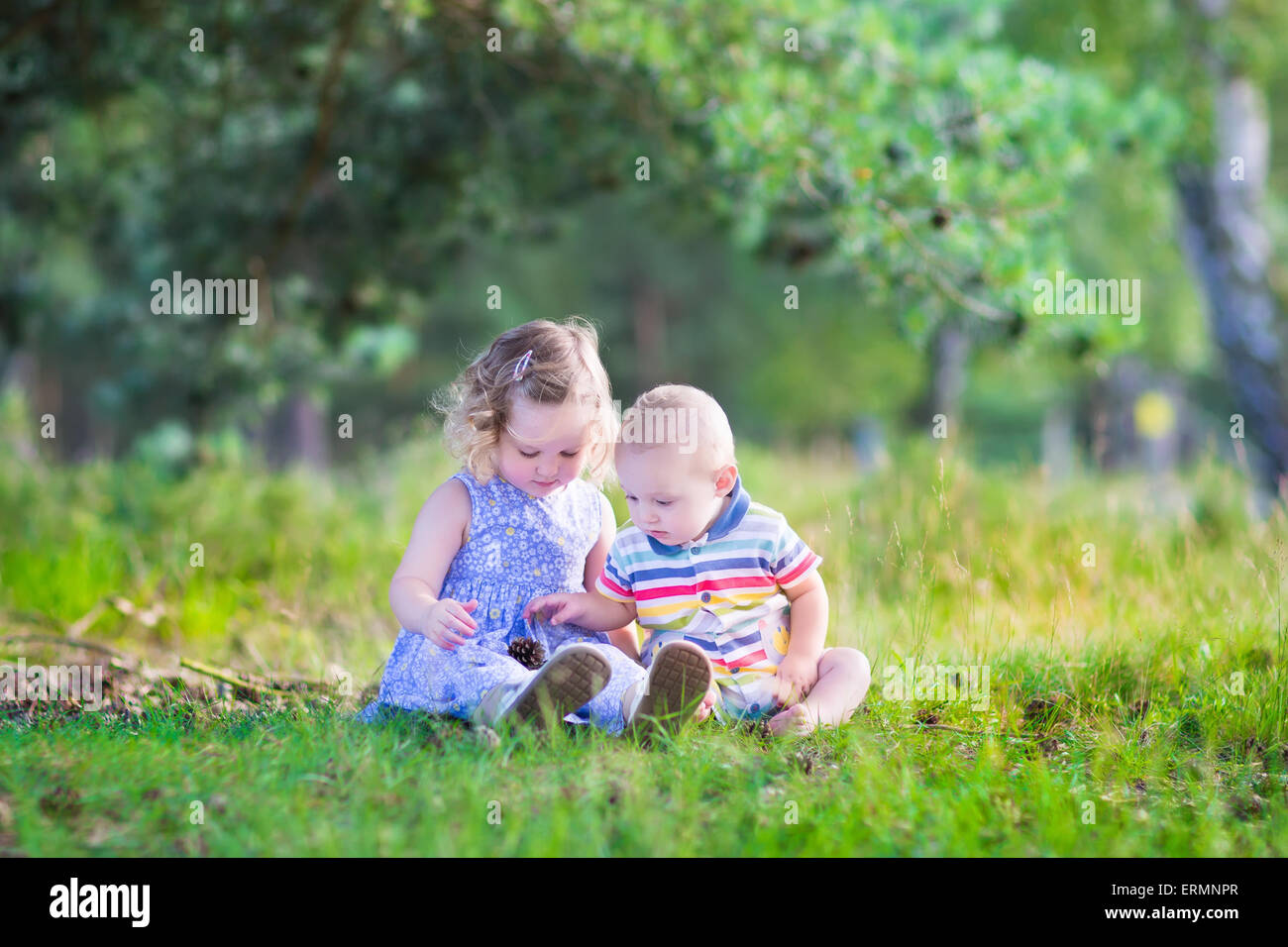 Happy little children, adorable toddler girl in a blue dress and a cute baby boy, brother and sister, playing with pine cones Stock Photo