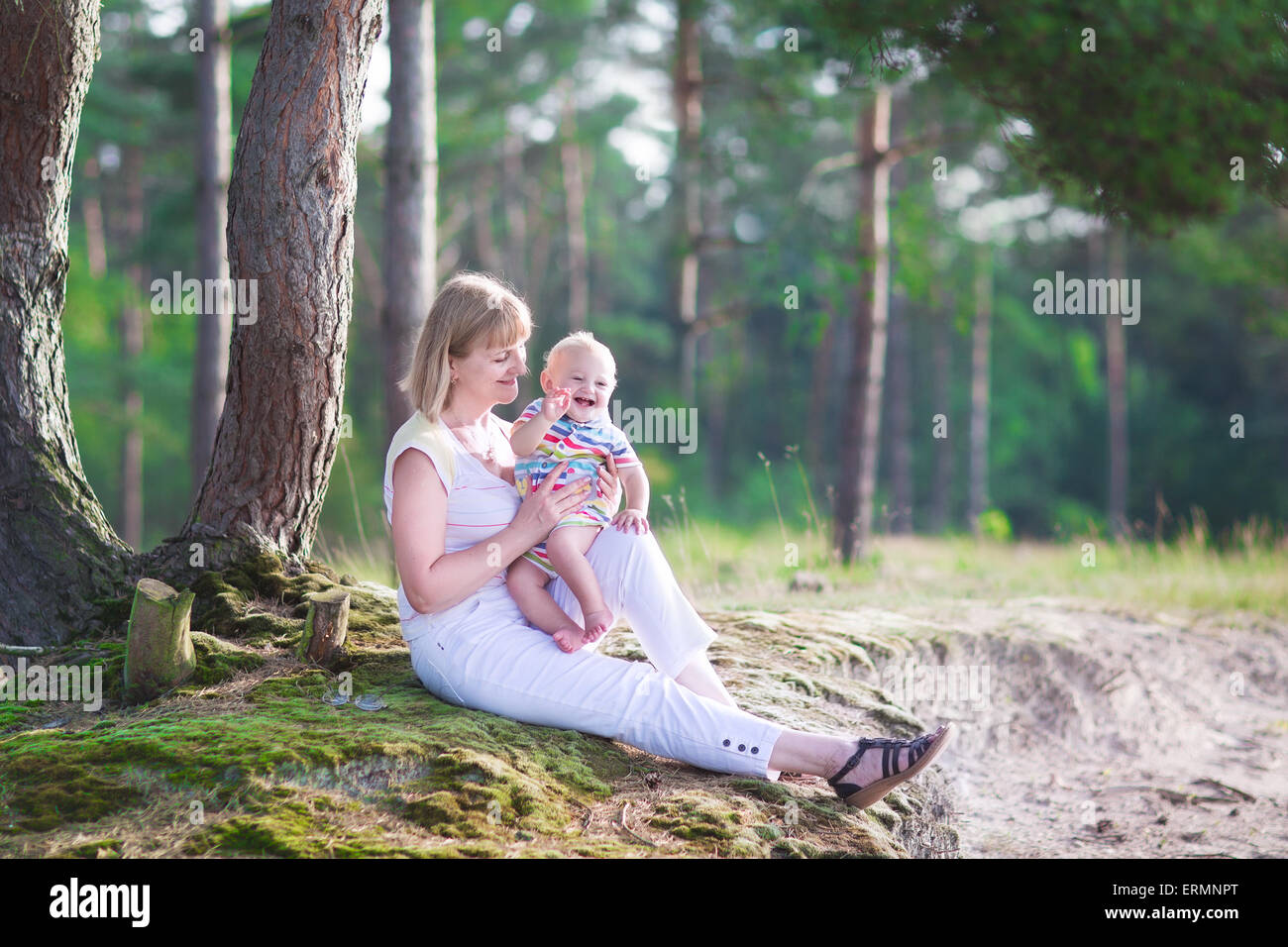 Happy active woman playing with a cute little child, adorable laughing baby boy, having fun enjoying hiking in pine wood forest Stock Photo