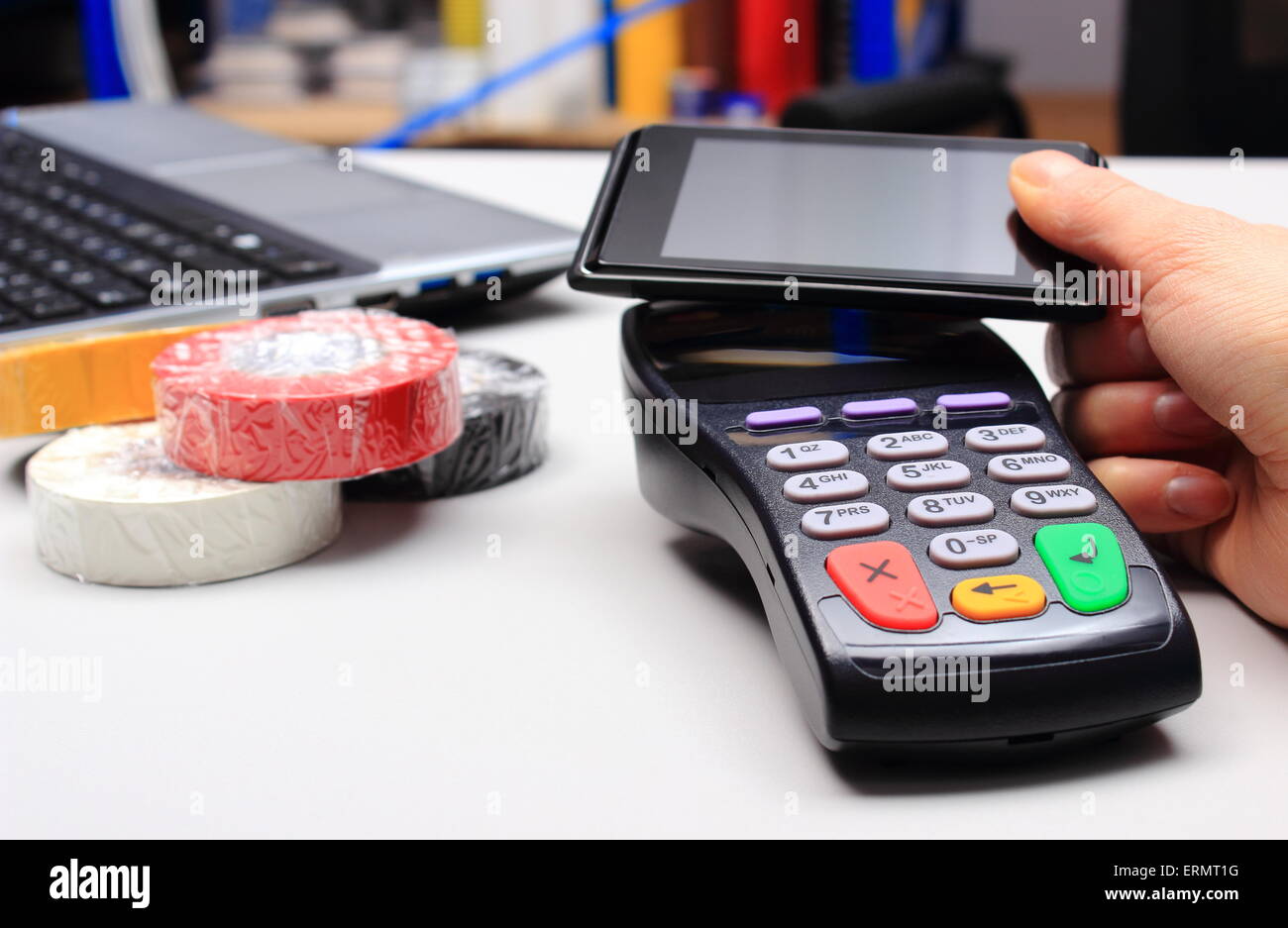 Hand of woman paying with NFC technology on mobile phone in an electrical shop, credit card reader, payment terminal, Stock Photo