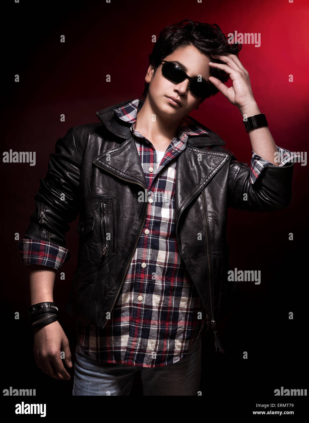 Handsome teen boy wearing stylish sunglasses and leather jacket over dark  red background, teenage fashion and style Stock Photo - Alamy