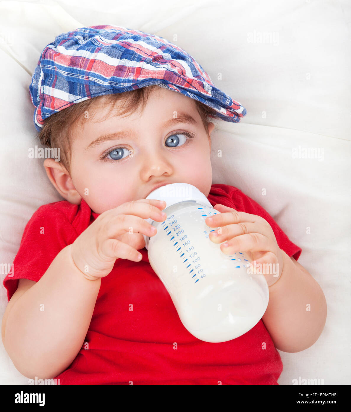 Portrait of cute little hungry baby boy drinking milk, lying on the bed