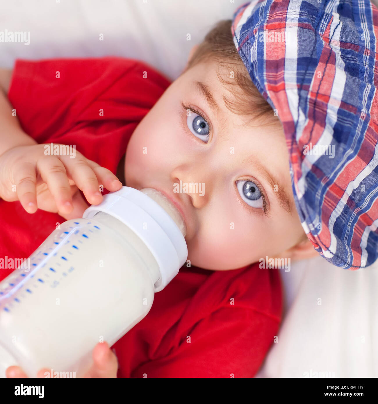 Portrait of cute little baby boy drinking milk, lying down on the bed