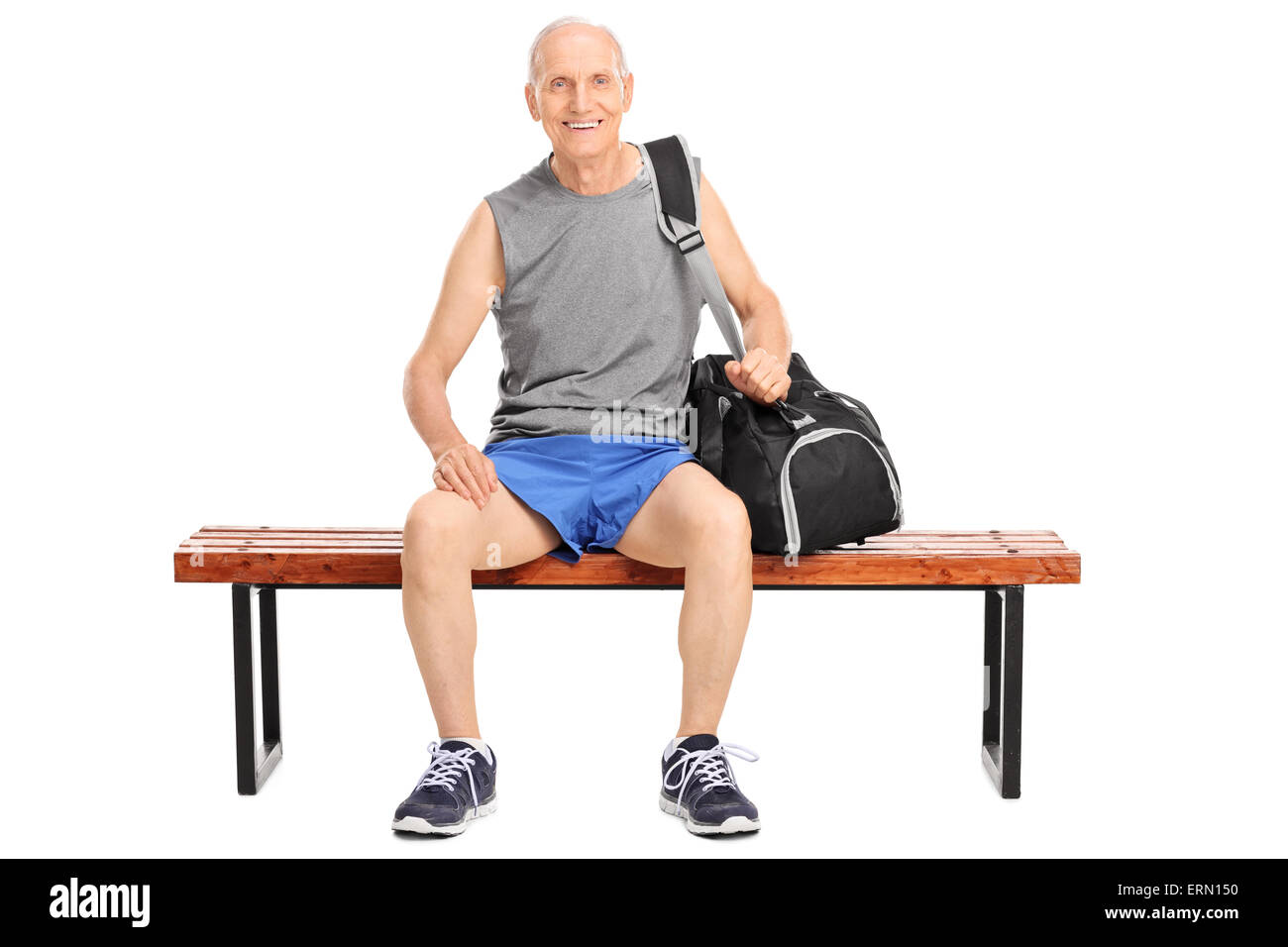Studio shot of a senior man sitting on a wooden bench in sportswear and carrying a sports bag isolated on white background Stock Photo