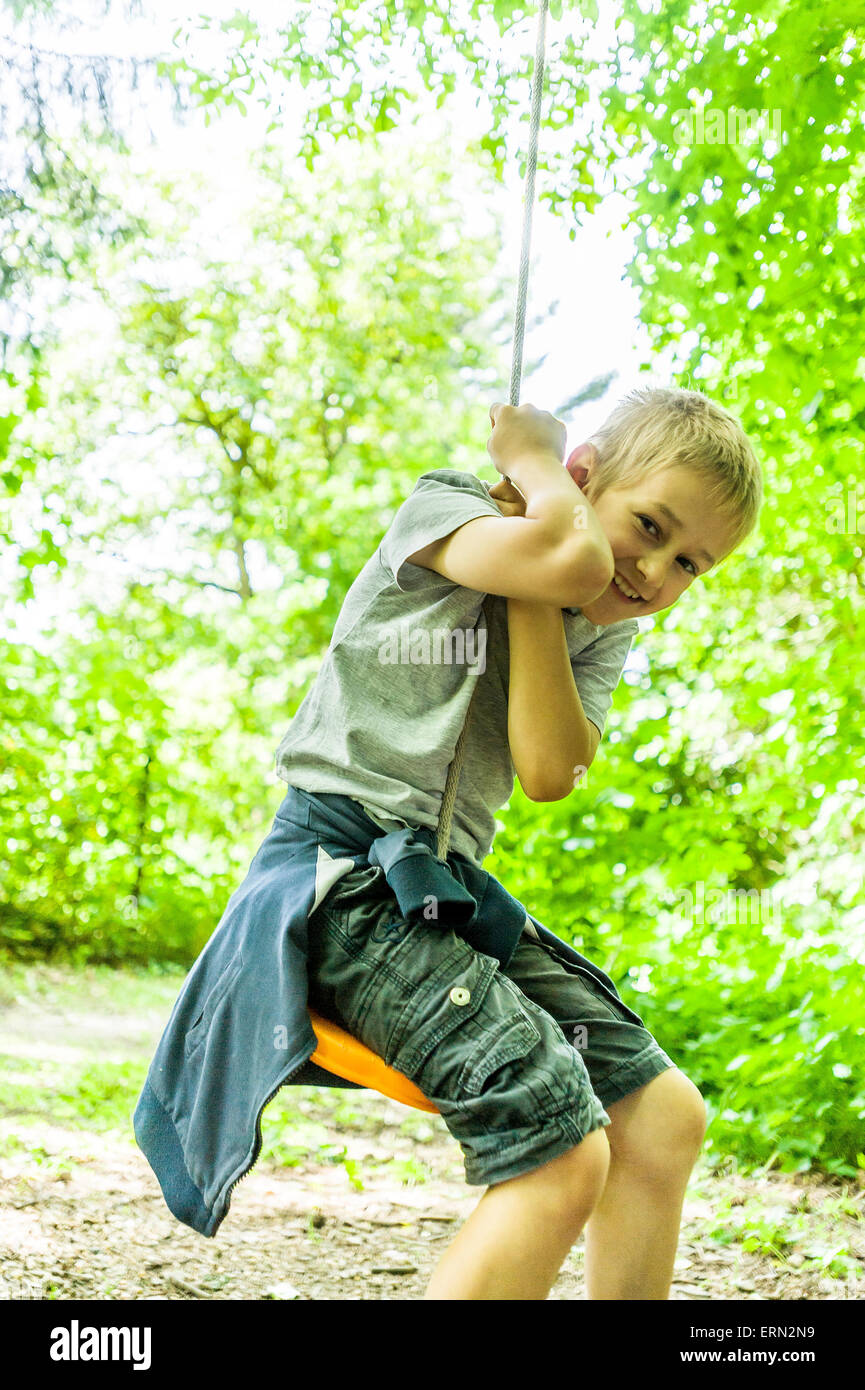 blond boy sitting at swing in wood Stock Photo
