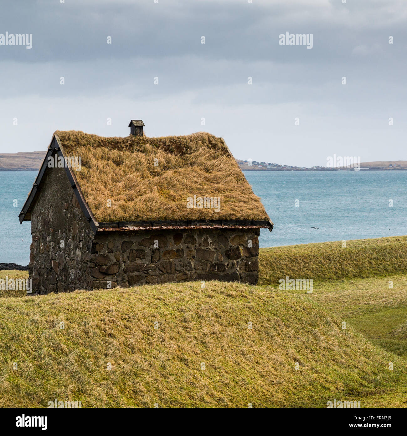 Traditional hut with a green grass roof with a backdrop of the Atlantic ocean and an island Stock Photo