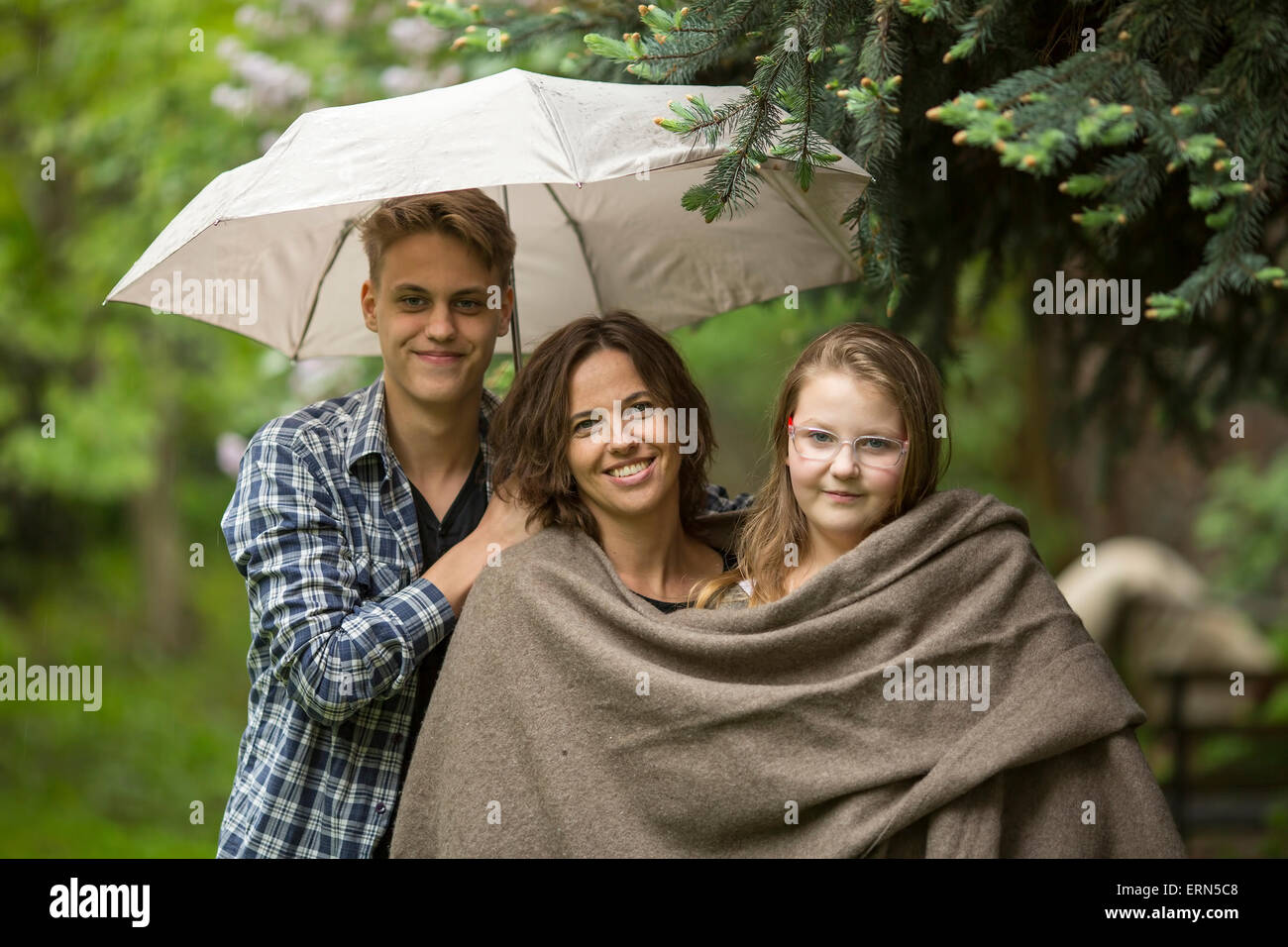 Woman with their adult children, daughter and son, in the Park under an umbrella. Stock Photo