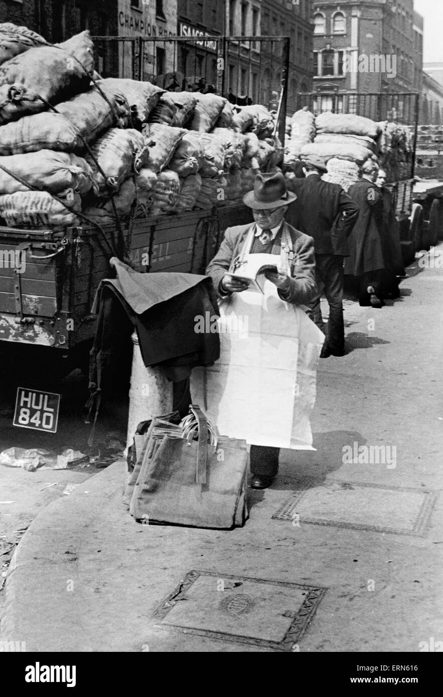 Covent Garden Market stall vendor stops to read a magazine. Circa 1955