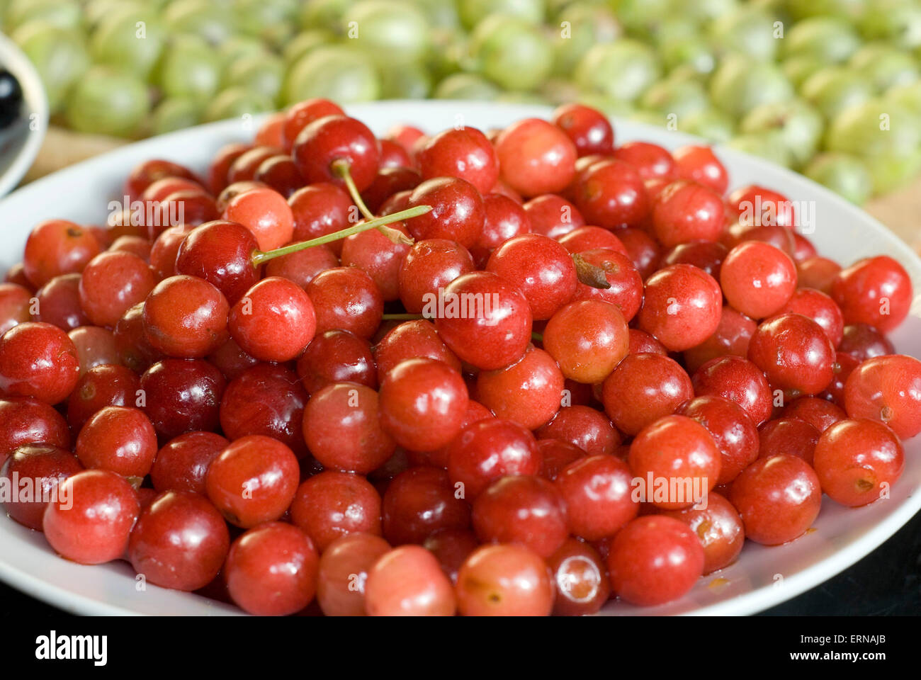 A bowl of red cherries with green gooseberries behind Stock Photo