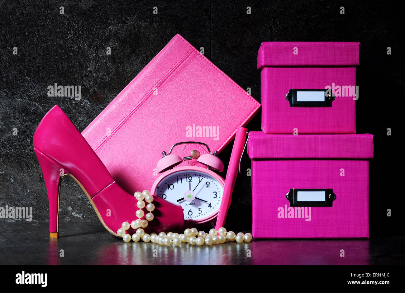 Ladies pretty pink female office desk with high heel shoe, clock, pen, stationery filing boses, pearls and diary organiser again Stock Photo