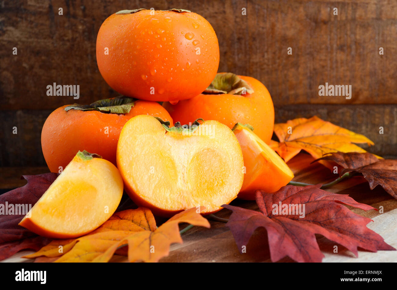 Persimmon Fall Stack of fresh Persimmons with cut slices on Autumn Fall leaves against ...