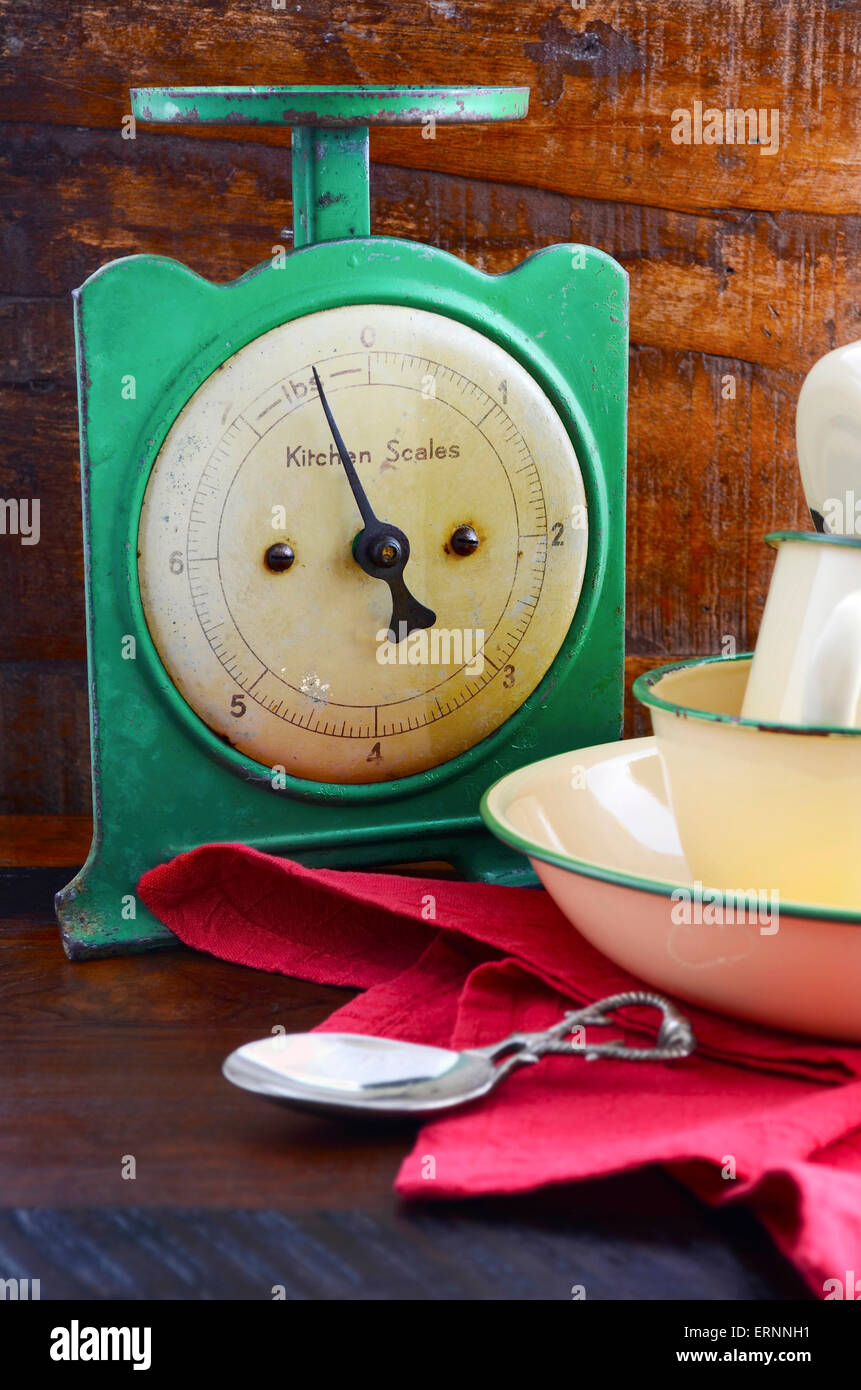Vintage kitchen scales and tin cups and pans on dark reclaimed wood background. Stock Photo
