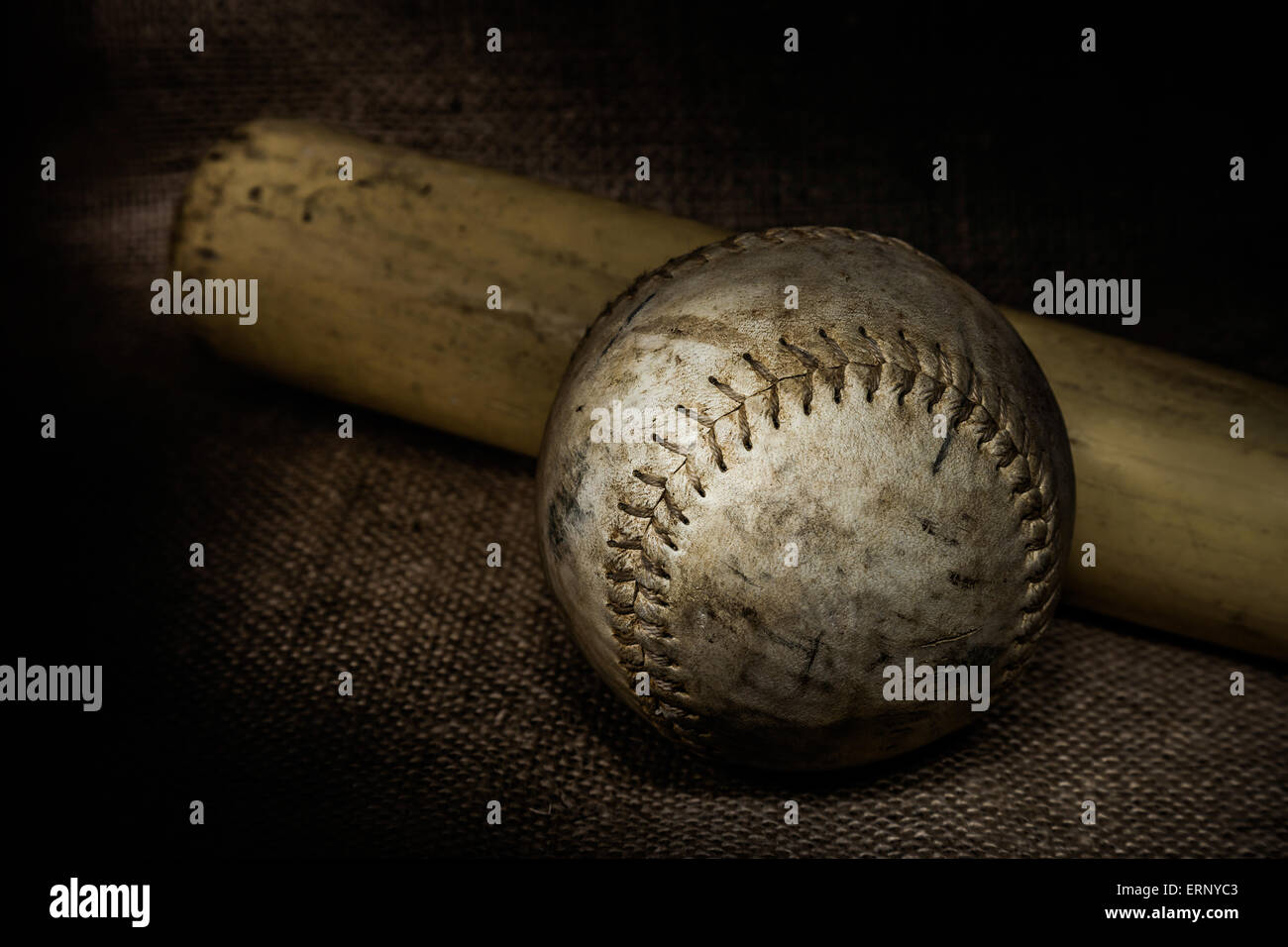 A worn softball and bat sit atop a burlap surface.  Image was lit using a lightpainting technique. Stock Photo