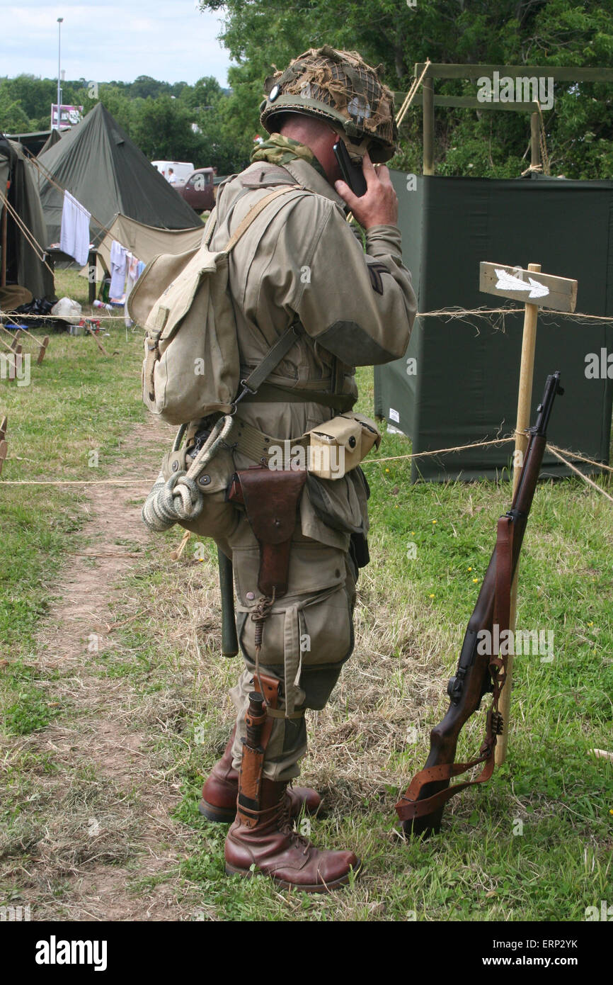 Carentan, Normandy, France. 6 June 2015. Reenactment groups recreate Camp Arizona complete with military vehicles, tents, memorabilia and costumes as part of the D-Day Festival 2015 and the 70th anniversary events for the end of WWII in 1945. Here 'old meets new' as a man dressed in the WWII uniform of a US paratrooper from 101 Airborne Division talks on his smart phone. Credit:  Daniel and Flossie White/Alamy Live News Stock Photo