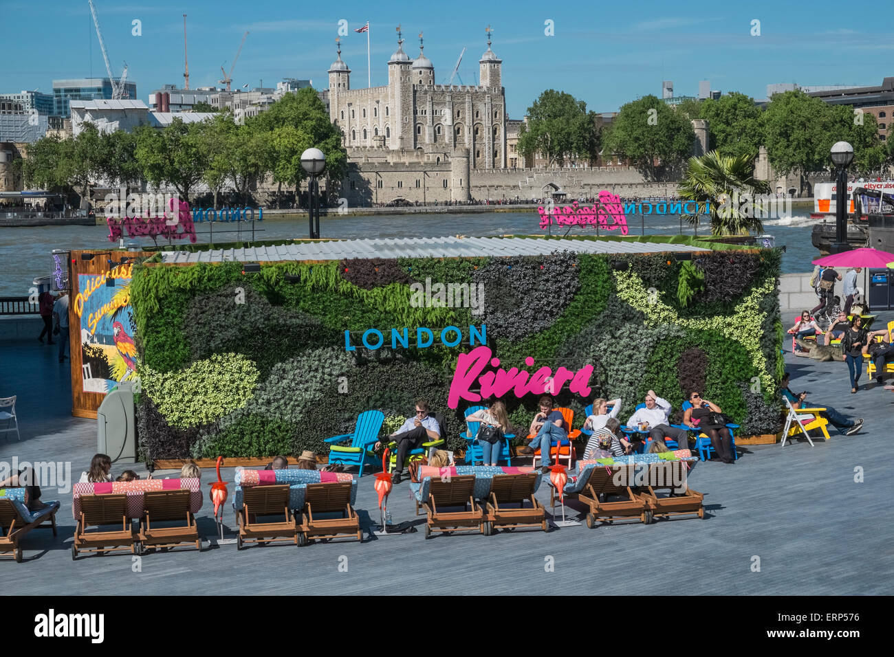 People relaxing in sunshine at London Riviera popup restaurant, with iconic Tower of London in background, Southbank, UK Stock Photo
