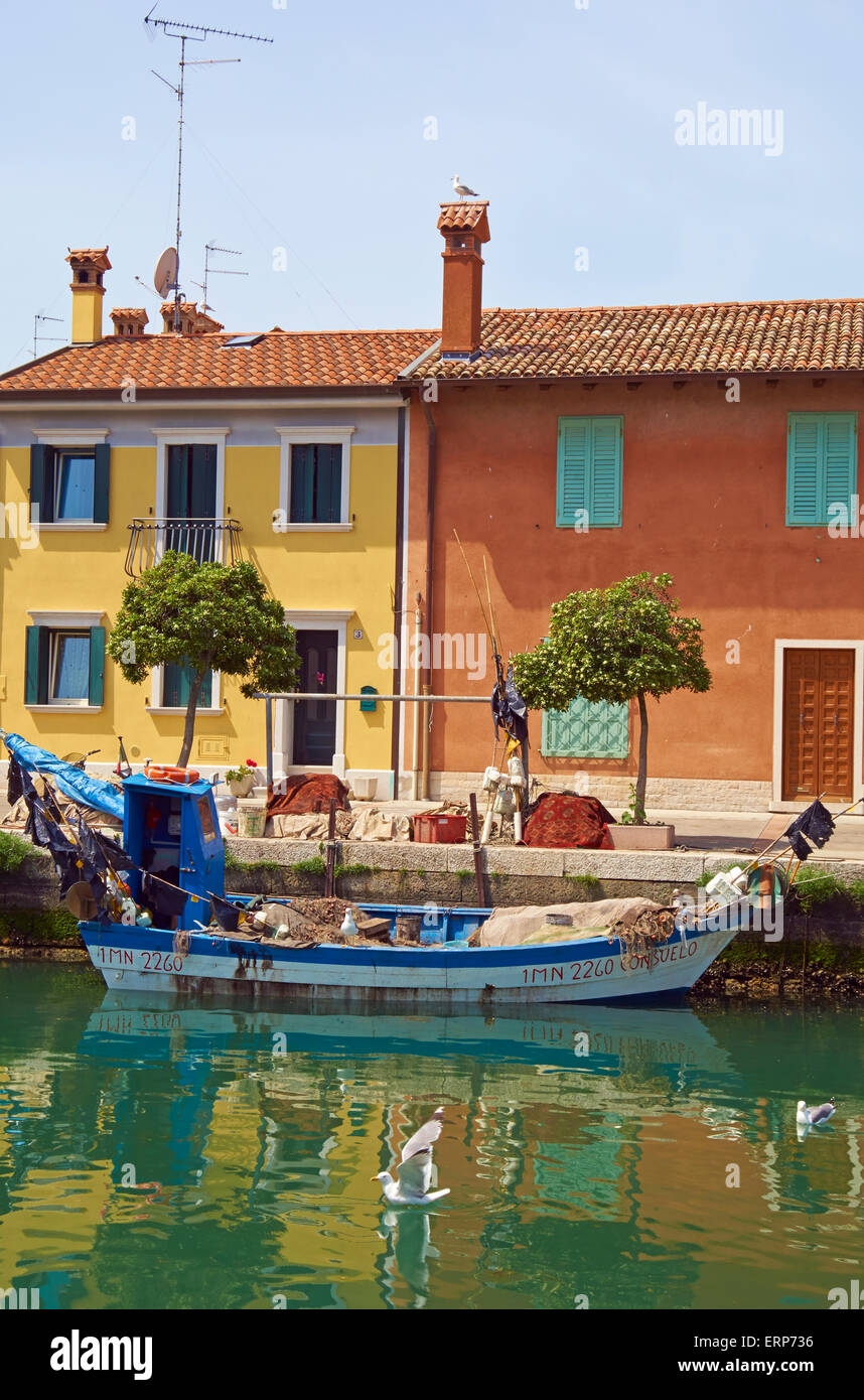 A fishing boat and coloured houses, Grado Canal, Grado, Friuli-Venezia Giulia, Italy. Stock Photo