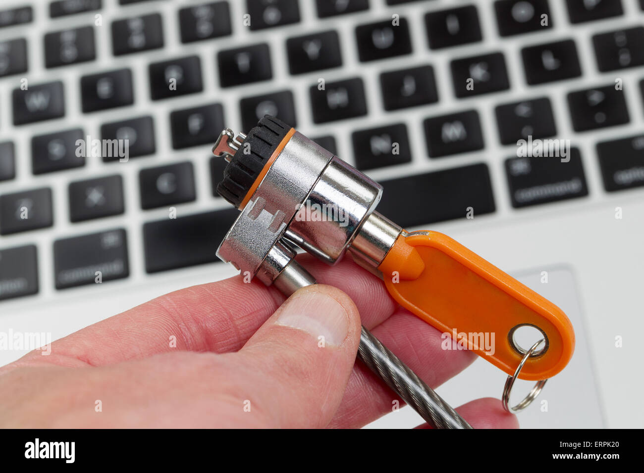 Close up of hand, focus on locking device, holding computer lock with keyboard in background. Stock Photo