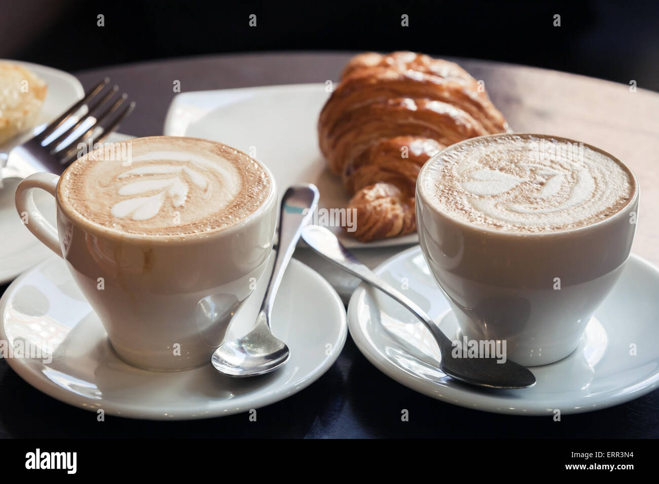 Cappuccino with croissant. Two cups of coffee with milk foam stands on a  table in cafeteria, vintage tonal correction photo filt Stock Photo - Alamy