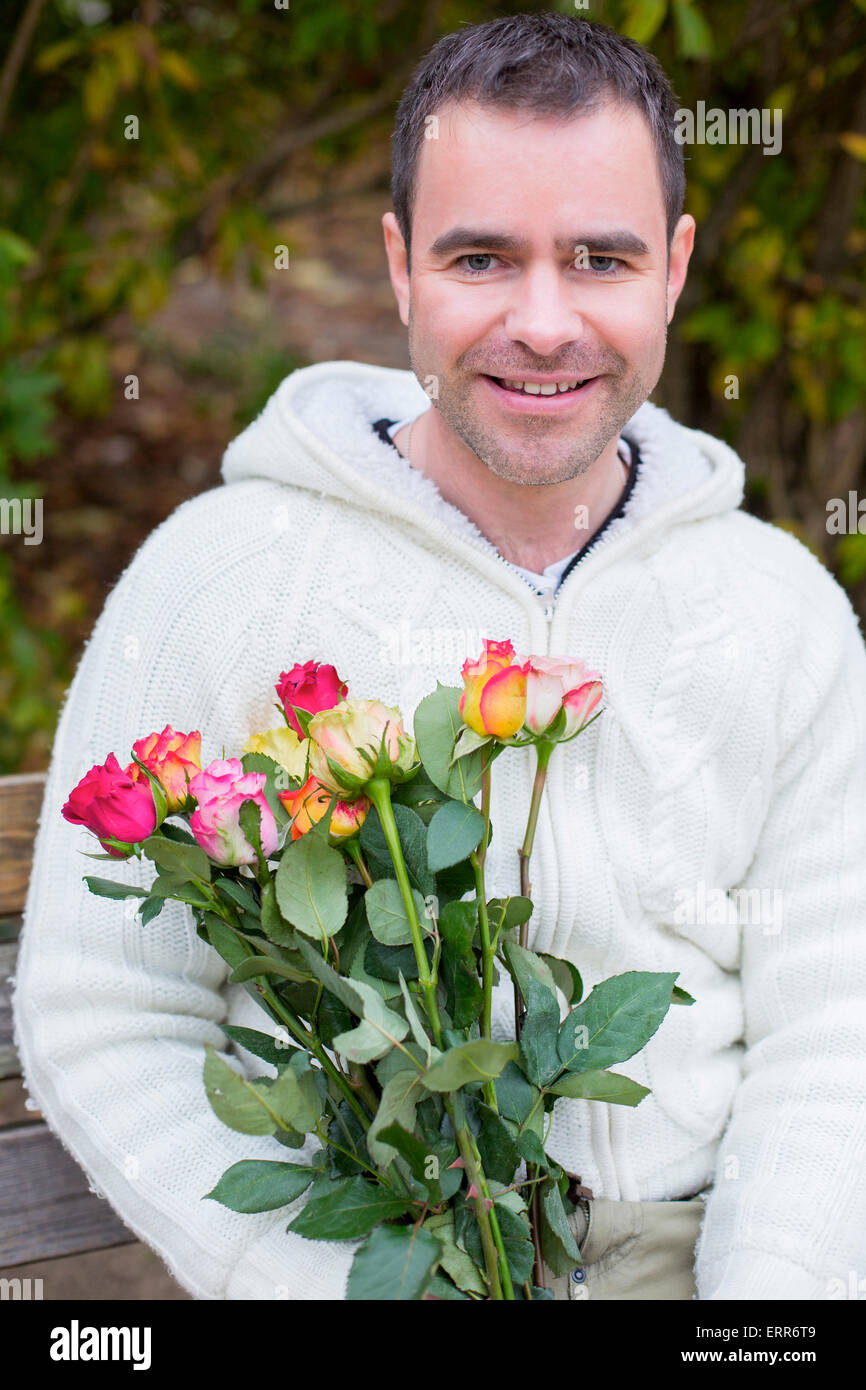 handsome man sitting outside on a bench with a bouquet of roses Stock Photo
