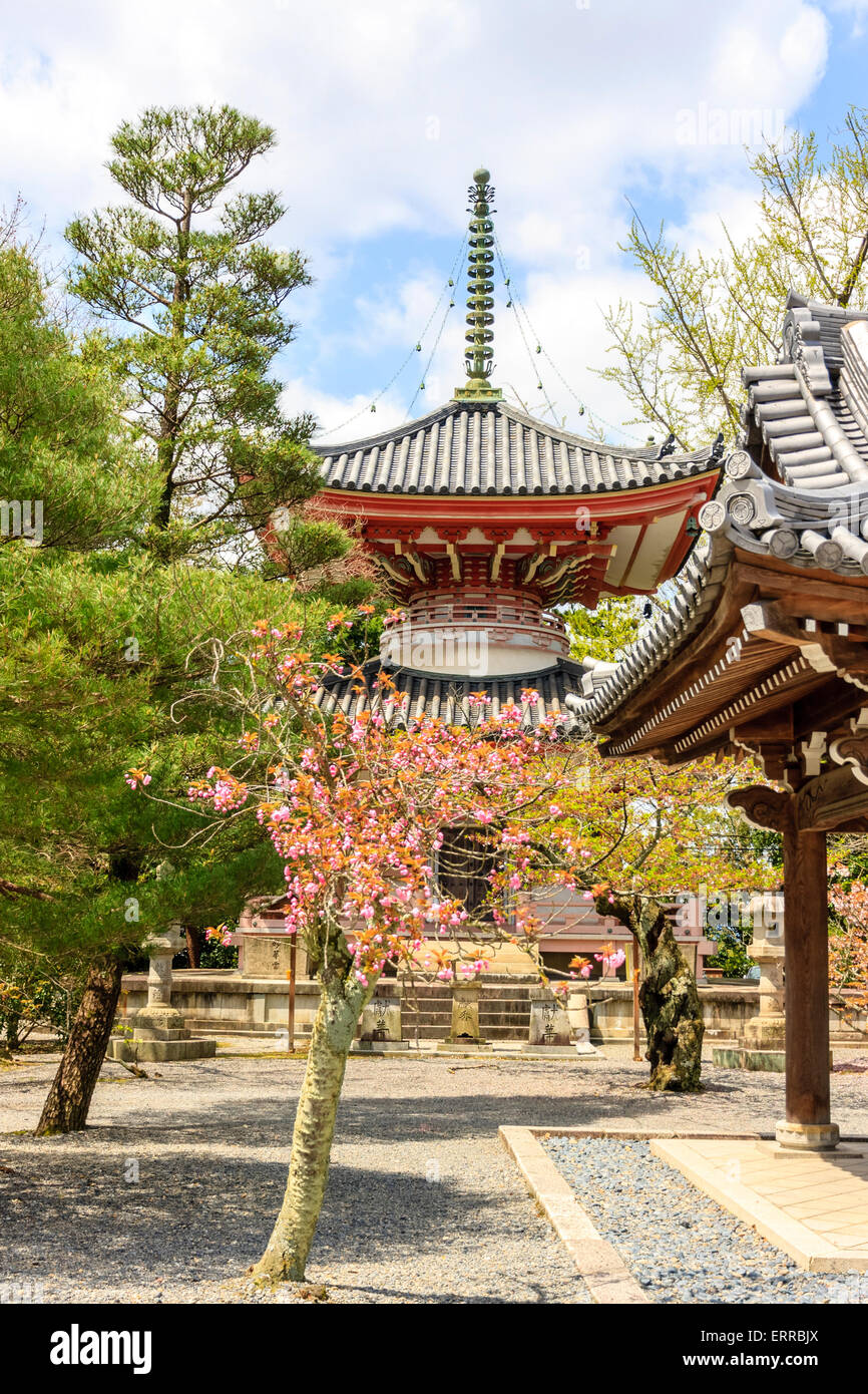 Japan, Kyoto, Chion-in Buddhist temple. Two story vermilion pagoda with trees and bushes around in the springtime. Cloudy blue sky background. Stock Photo