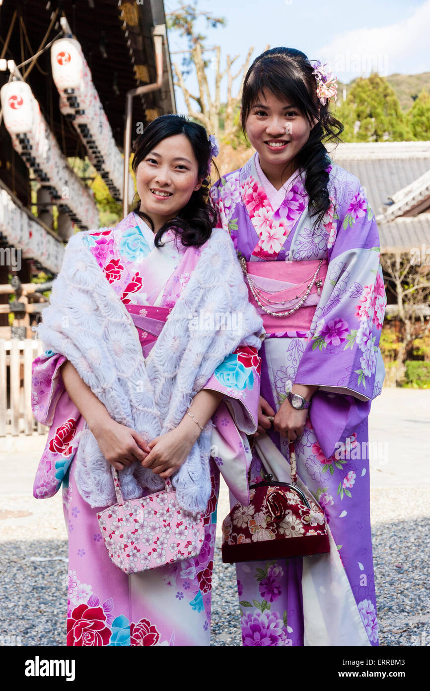 Two young Chinese women standing posing and smiling at viewer at a Japanese  shrine in Kyoto. Both wearing pink and purple kimono with flower designs  Stock Photo - Alamy