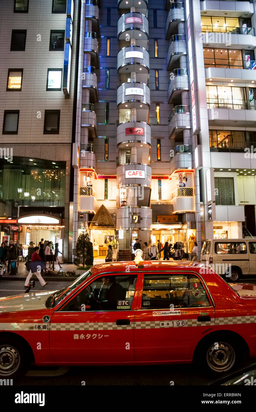 Exterior of the Cafe de Ginza Miyuki-kan in the distinctive W facade shape of the Ginza Act Building in Tokyo at night. Red taxi in foreground. Stock Photo