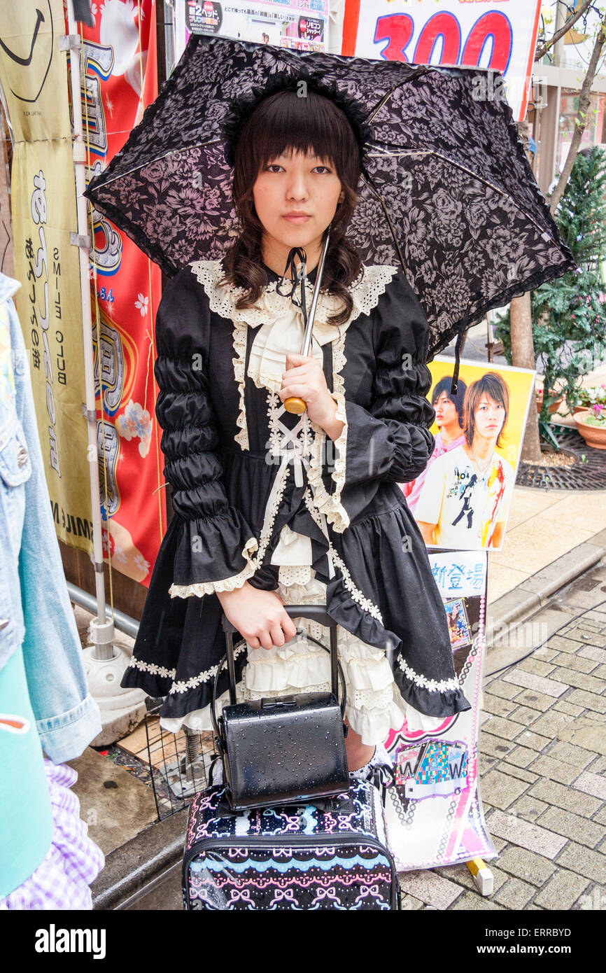 Harajuku, Tokyo. Japanese young woman dressed in Goth Lolita style in black Victorian maid costume and holding black lacy umbrella. Eye-contact. Stock Photo