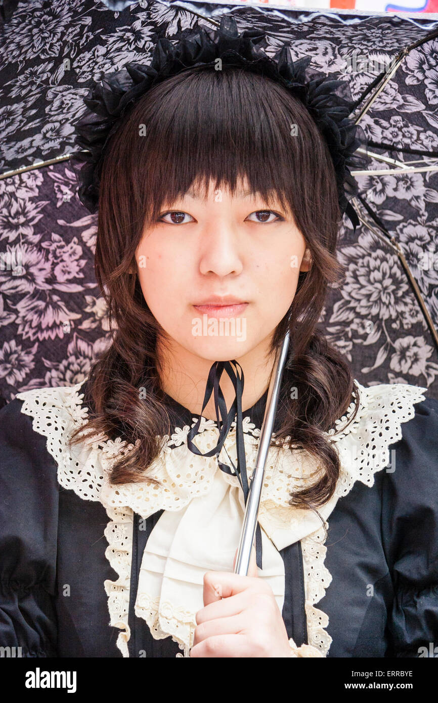 Harajuku, Tokyo. Face, Japanese young woman dressed in Goth Lolita style in black Victorian maid costume and holding black lacy umbrella. Eye-contact. Stock Photo