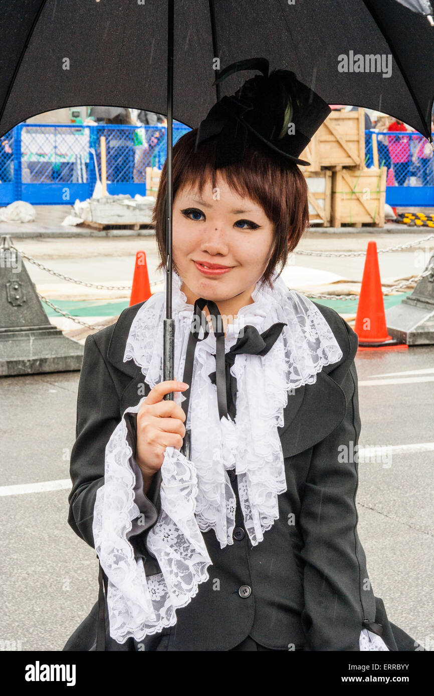 Harajuku, Toyko. Japanese young woman dressed up in 'Sweet Lolita' Classic Lolita style Victorian maid outfit and holding black umbrella, smiling. Stock Photo