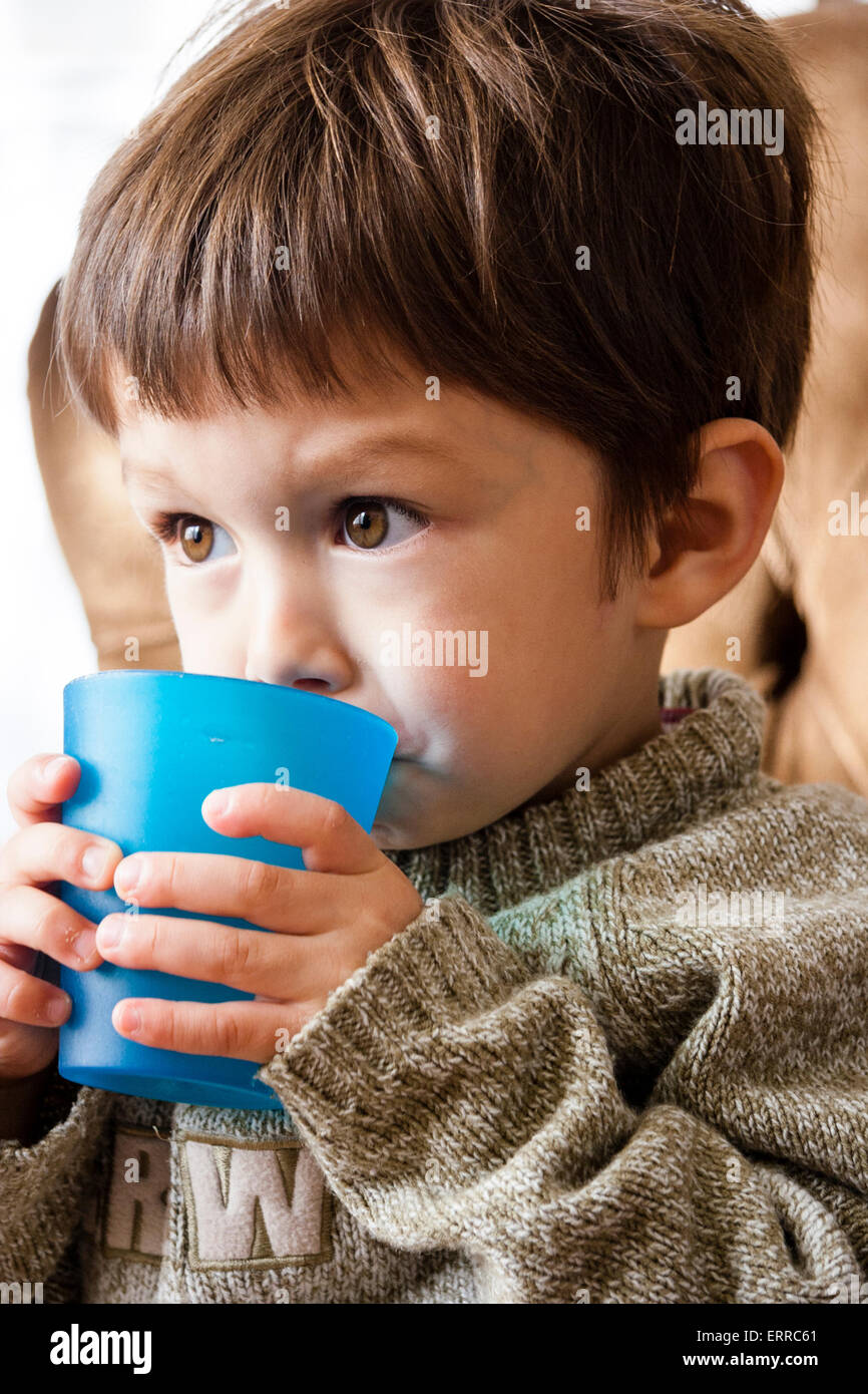 Caucasian child, boy, 3-4 year old, sitting on settee, holding in hand a  plastic cup and drinking from it while watching something in front Stock  Photo - Alamy