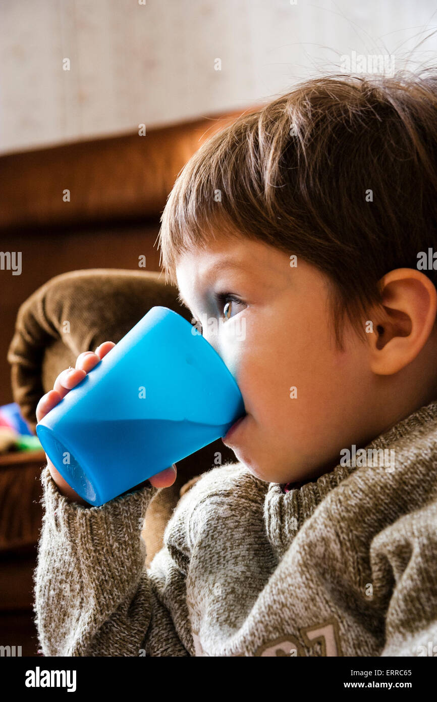 Caucasian child, boy, 3-4 year old, sitting on settee, holding in hand a  plastic cup and drinking from it while watching something in front Stock  Photo - Alamy