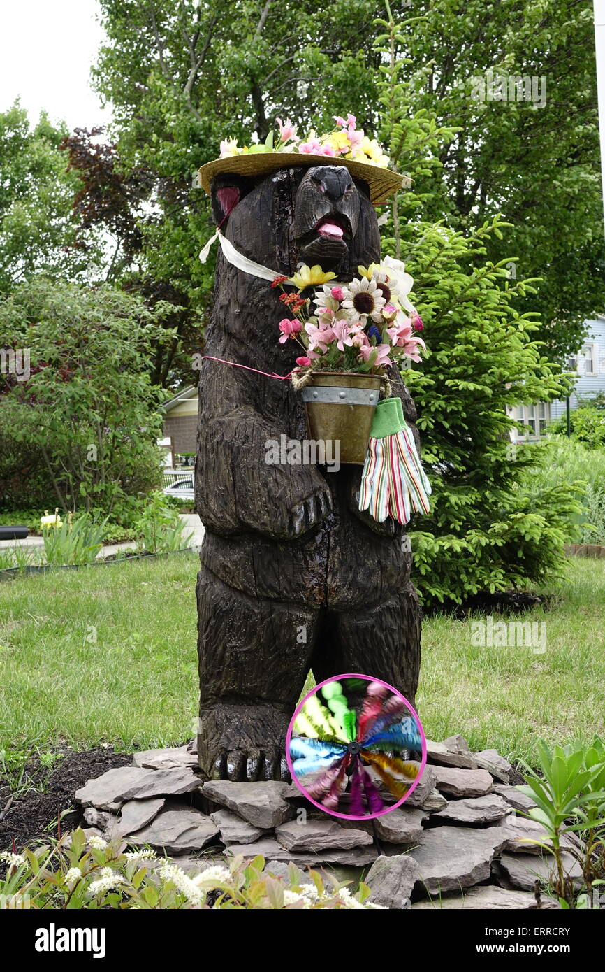 Wooden bear adorned with flowers and gardening gloves in front of Free