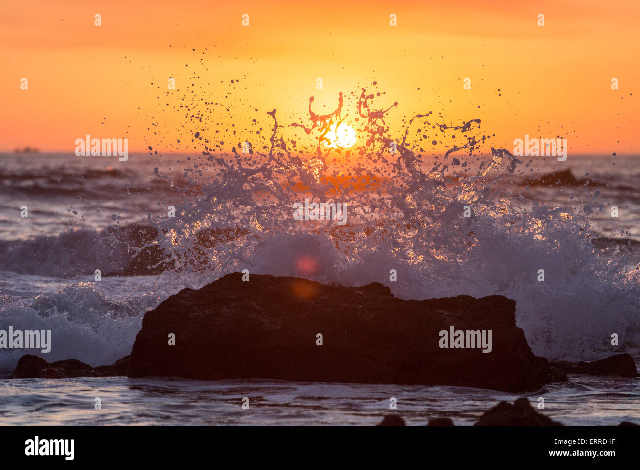 crashing wave on rock with sunset in background Stock Photo - Alamy