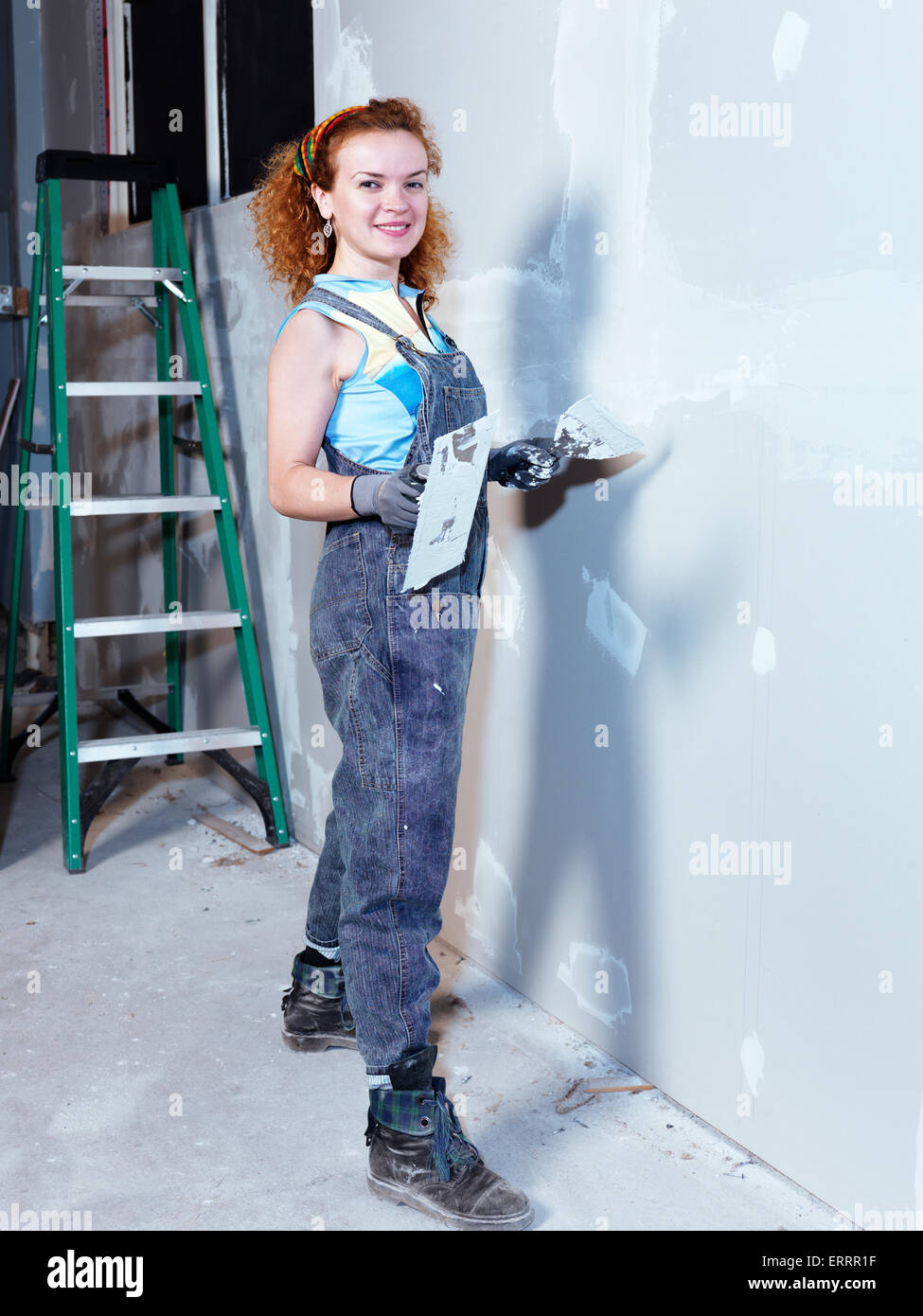 Portrait of a smiling young woman with a trowel and putty knife patching up drywall renovating interior Stock Photo