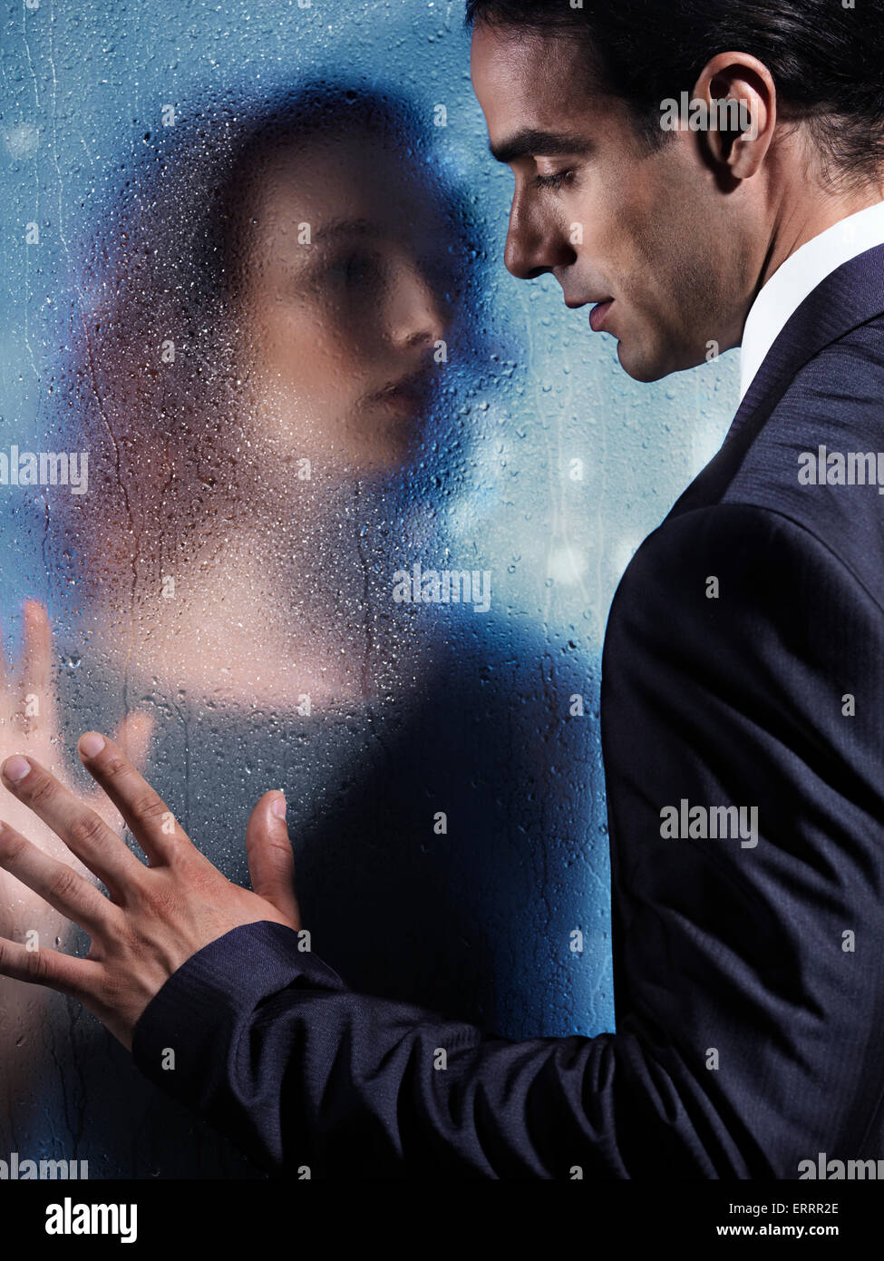 Emotional portrait of a young man and a woman separated by a wet glass pane. Couple relationship concept. Stock Photo